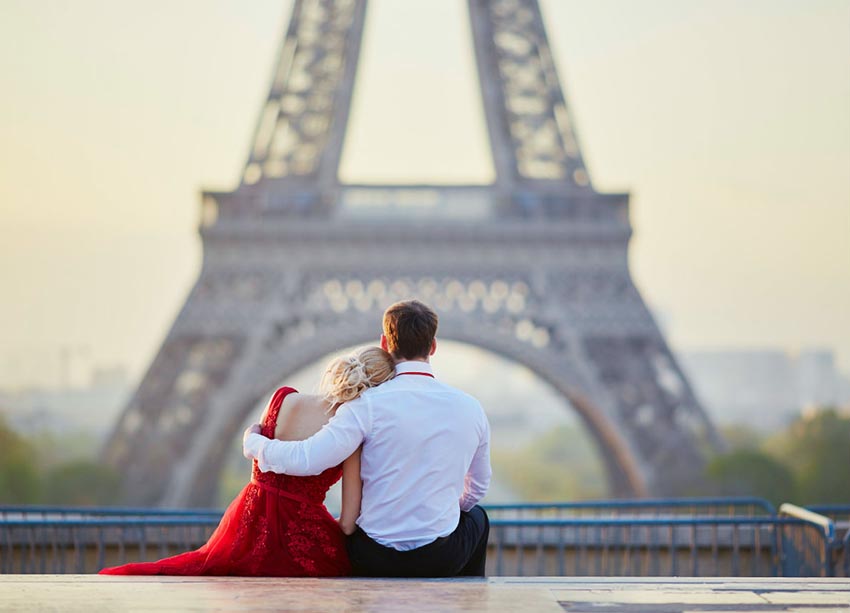 Zamilovaná dvojica sediaca pred Eiffelovou vežou v Paríži