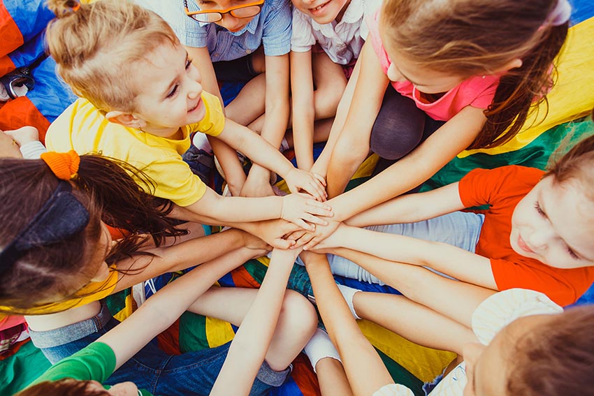 Skupina veselých detí vo farebných tričkách ako sa v kruhu držia za ruky