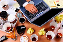neuprataný pracovný stôl s notebookom a množstvom pohárov od kávy