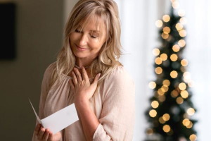 Staršia žena číta vianočnú pohľadnicu a usmieva sa