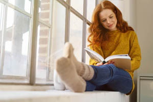 ryšavé dievča číta knihu na parapete